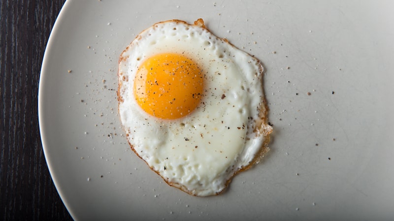 木のテーブルの上の白い皿の上の目玉焼き